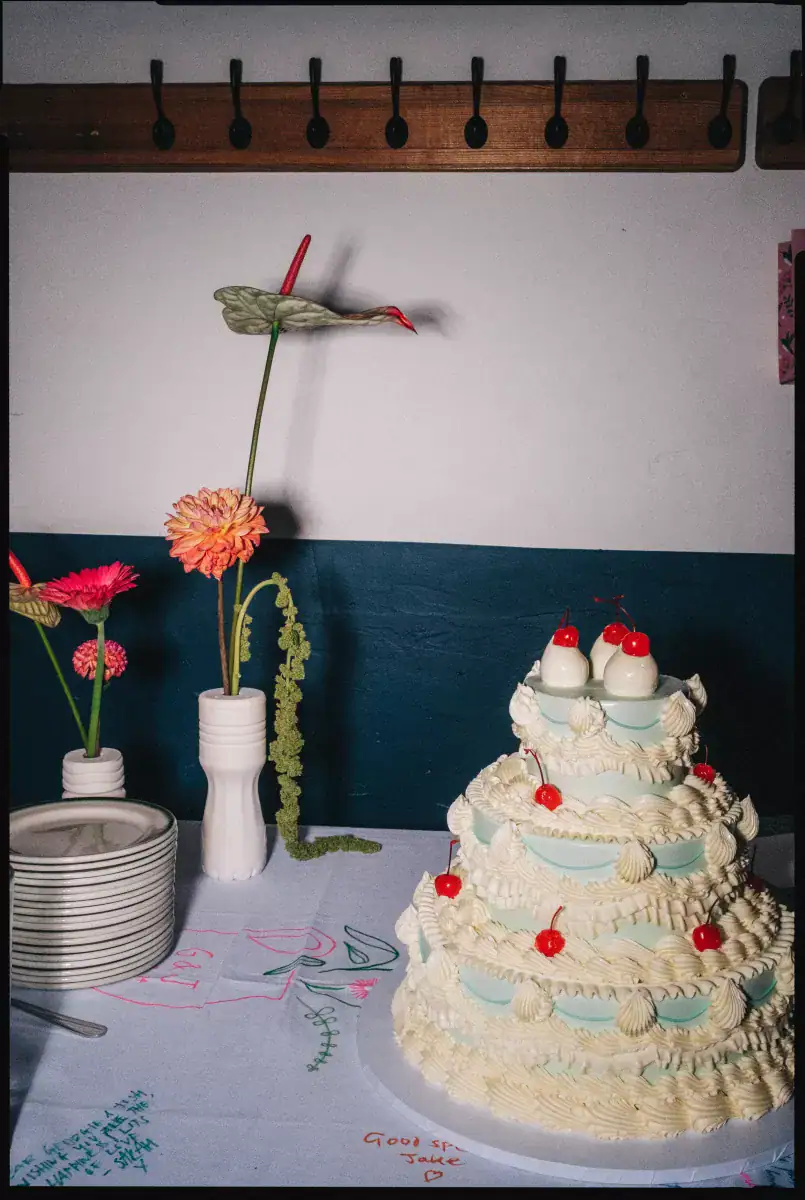 Tiered cream wedding cake with pale blue layers and red cherries beside stemmed flowers at Camberwell Arms