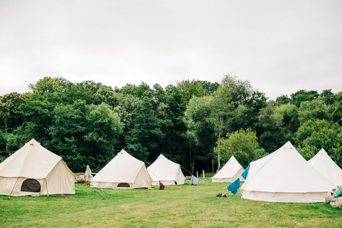Several large white canvas tents are set up on a grassy field, surrounded by dense green trees under a cloudy sky, creating the perfect setting for relaxed festival wedding vibes or inspiring garden festival wedding ideas.