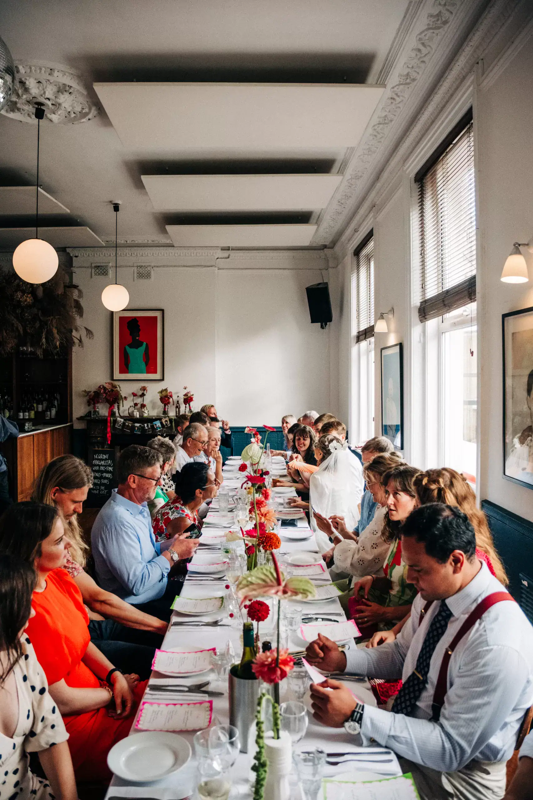 Guests chat and read menus along one long table of bright flowers in the high-ceilinged upstairs room at Camberwell Arms