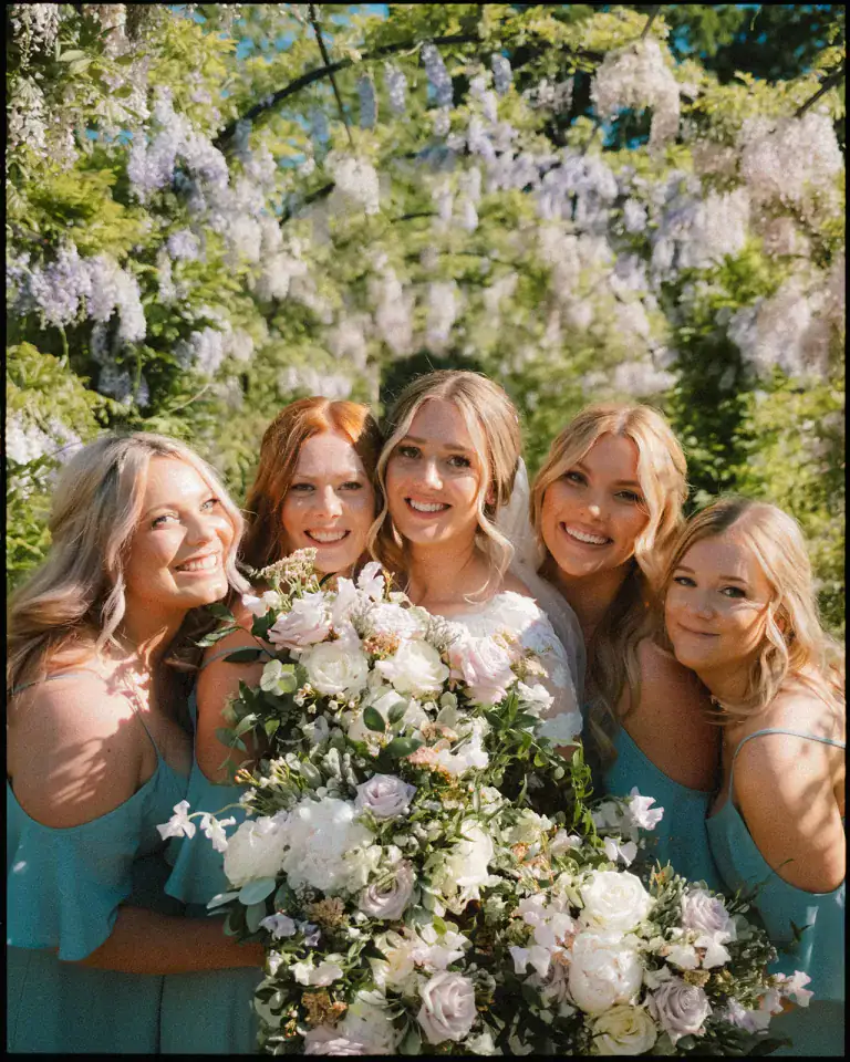 bride and bridesmaids pose with flower bouquets in front of wisteria arch at thorpe garden summer wedding