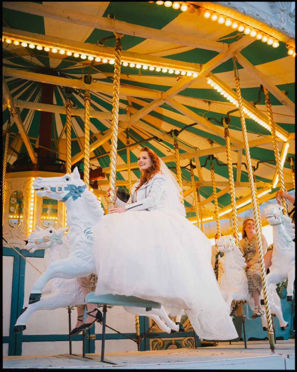 Bride riding carousel horse at Preston Court wedding in Kent during evening celebrations.