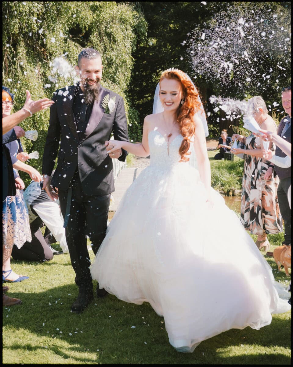 Bride and groom walking through confetti throw at Preston Court wedding in Kent.
