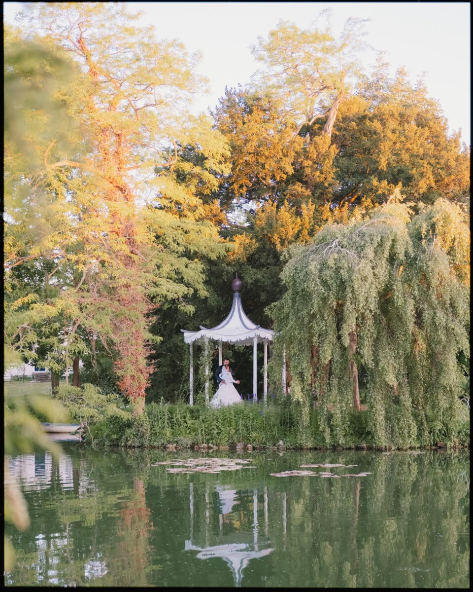 Bride and groom at Preston Court pagoda by the lake during golden hour.