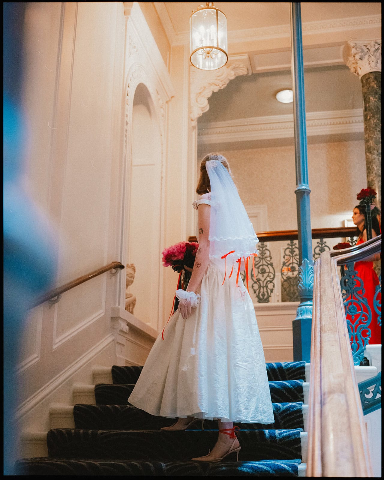 A timeless moment at The Grand Brighton — the bride descends the staircase, bouquet in hand, ready to leave for her Town Hall wedding ceremony. Bride in vintage-style dress walking down the staircase at The Grand Brighton before her wedding ceremony at Brighton Town Hall.