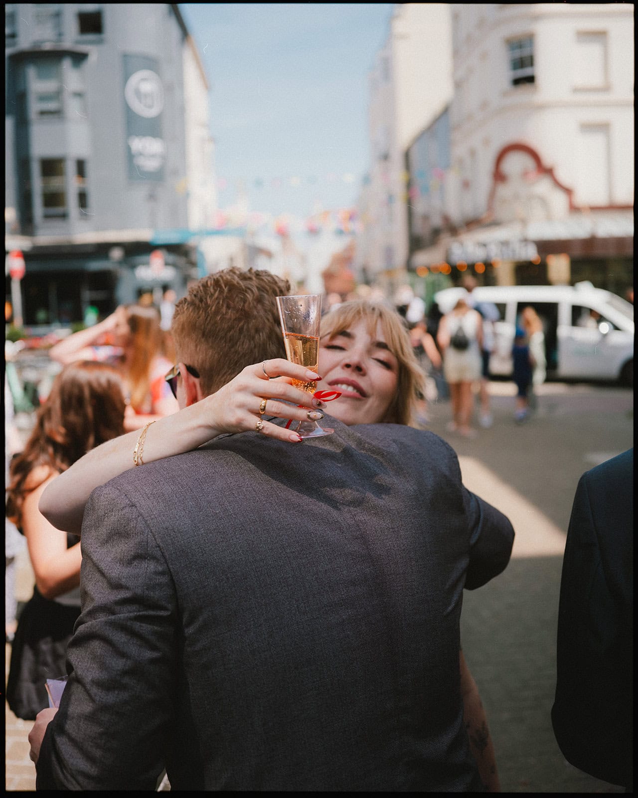 Bride hugging a guest with a glass of champagne outside Brighton Town Hall after the wedding ceremony.