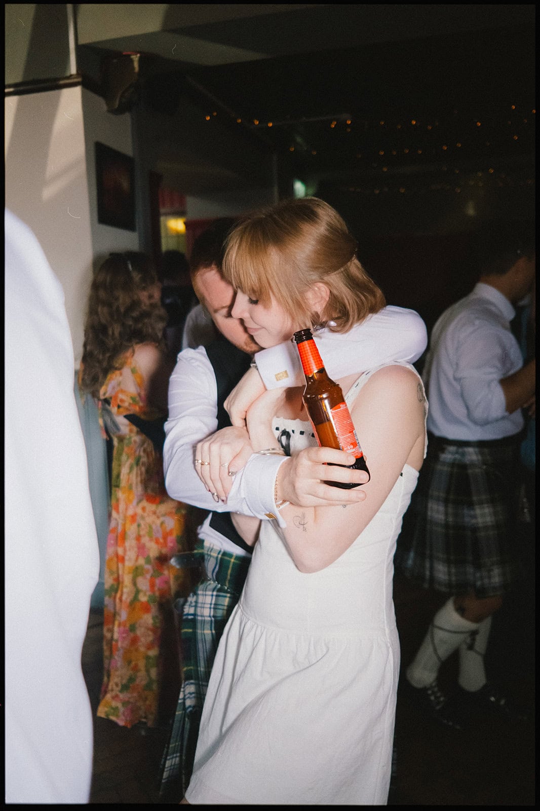 An intimate candid moment on the dance floor — the bride and groom share a hug with a beer in hand at The Garden Bar in Hove, surrounded by guests as the evening celebrations unfold. Bride and groom hugging on the dance floor at The Garden Bar Hove during their wedding reception, holding a beer and surrounded by dancing guests.