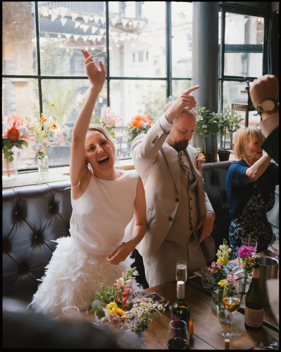 Bride and groom smiling and raising their arms while arriving at the wedding breakfast at The Depot N7 in London.