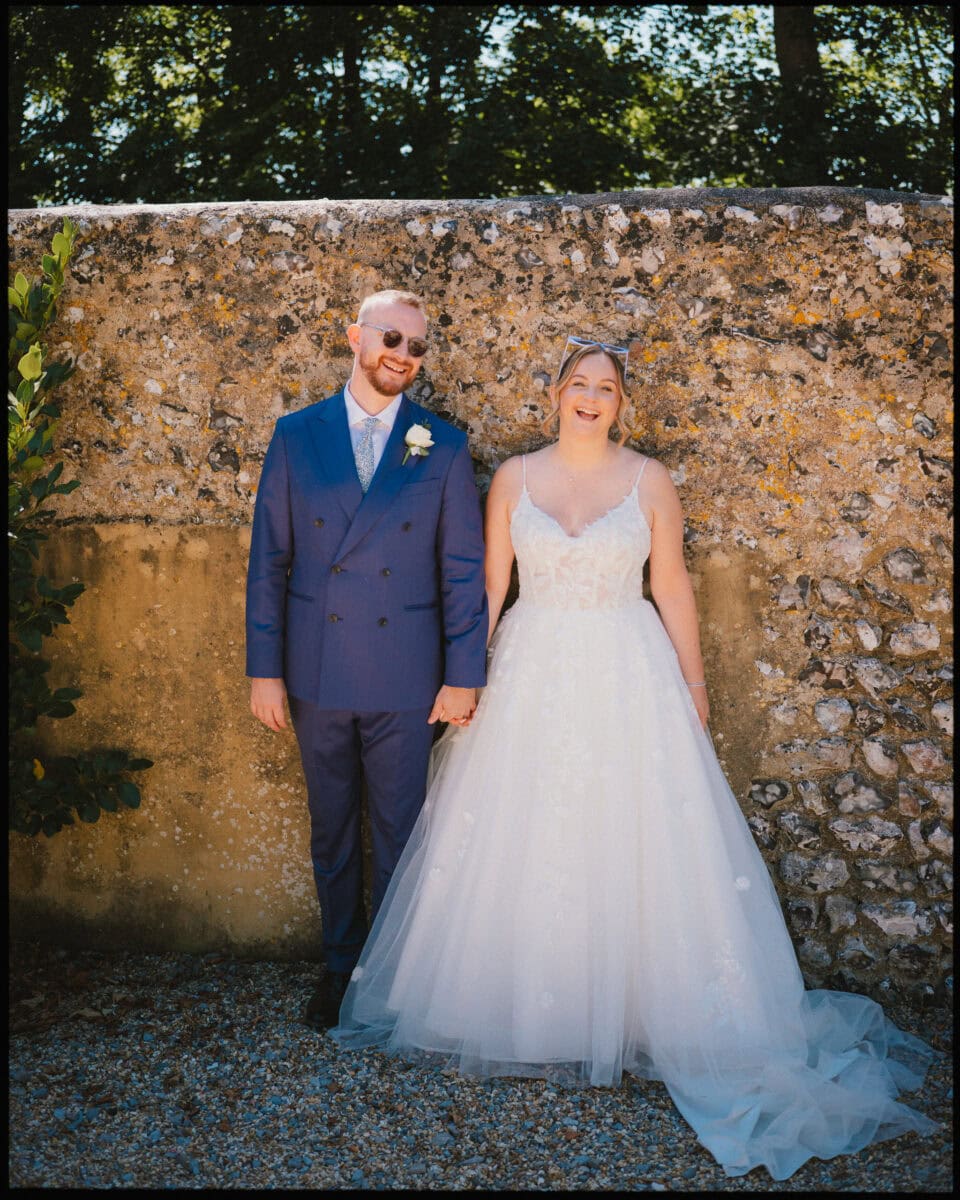 Bride and groom laughing together in front of a flint wall during their wedding at Cissbury Barns in West Sussex.