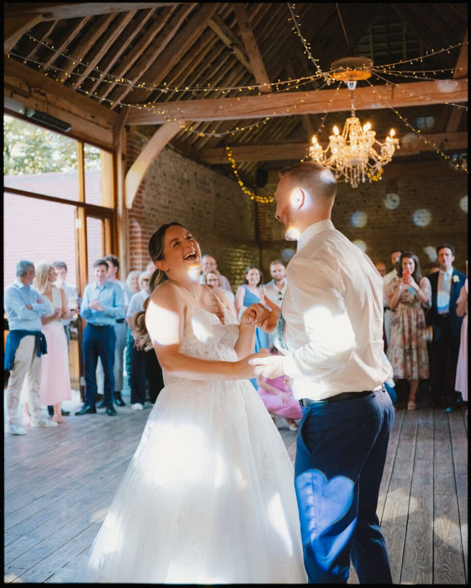 Bride and groom sharing their first dance, laughing together under fairy lights and a chandelier at Cissbury Barns wedding reception in West Sussex.