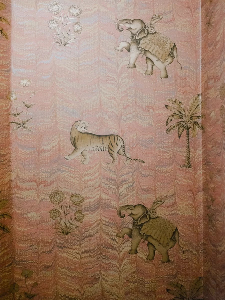 Illustrated wallpaper with a soft pink and orange marbled background, featuring two decorated elephants, a tiger, palm trees, and flowers in a traditional style.