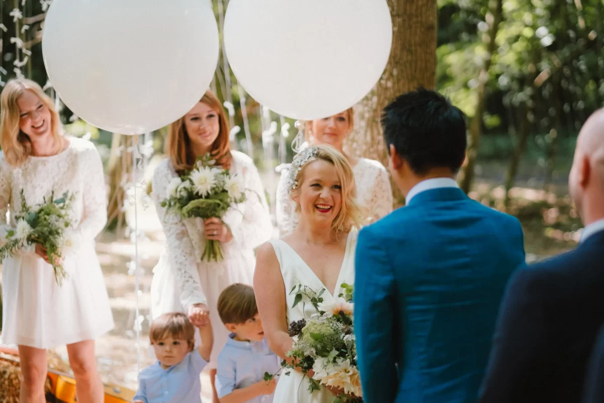 bride smiling during ceremony with white balloons in the woods at exclusive woodland wedding venue paper mill kent