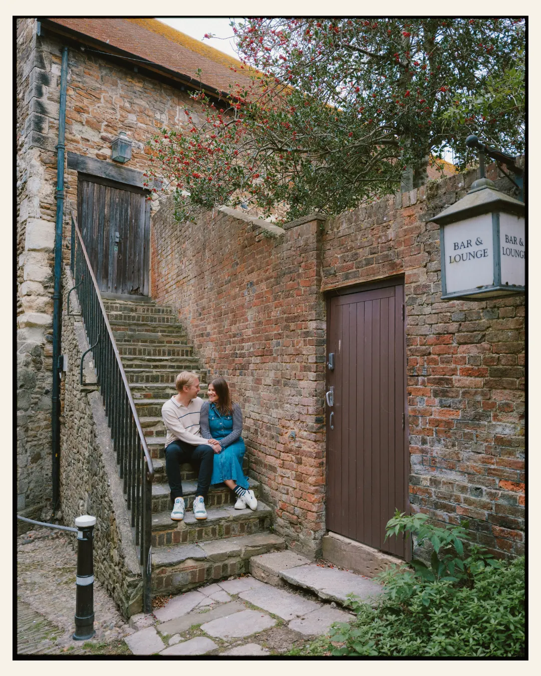 american couple sat on cobbled street steps in an alley in the ancient town of rye for their engagement shoot ahead of their destination wedding