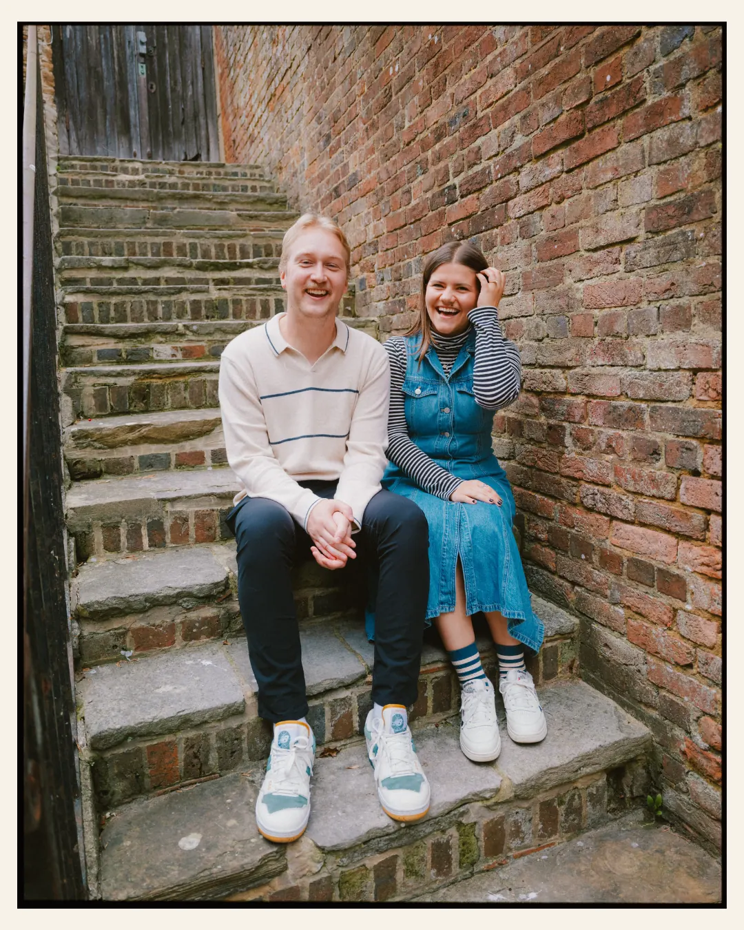 american couple sat in front of tudor building on steps in a candid moment in the ancient town of rye for their engagement shoot ahead of their destination wedding