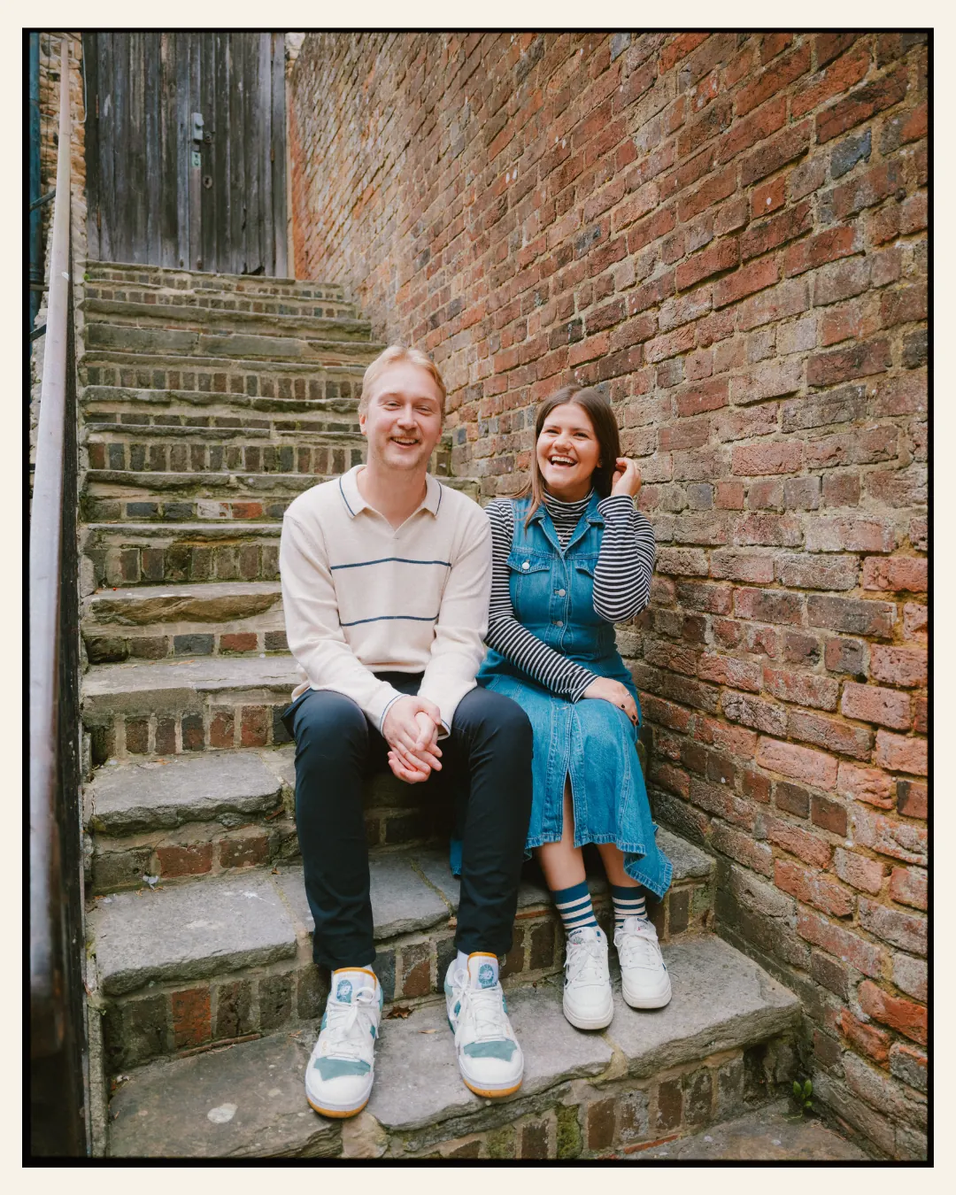 american couple sat in front of tudor building on steps in a candid moment in the ancient town of rye for their engagement shoot ahead of their destination wedding