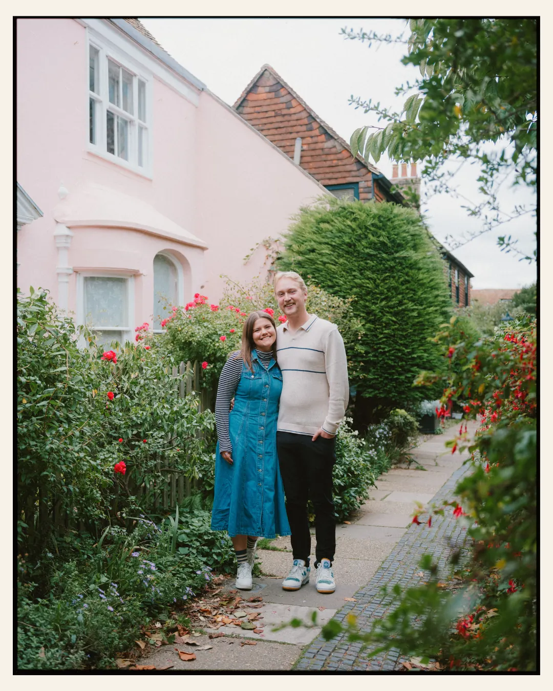 american couple standing in front of pastel old building in the ancient town of rye for their engagement shoot ahead of their destination wedding