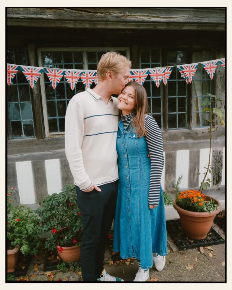 american couple standing in front of tudor building in the ancient town of rye for their engagement shoot ahead of their destination wedding