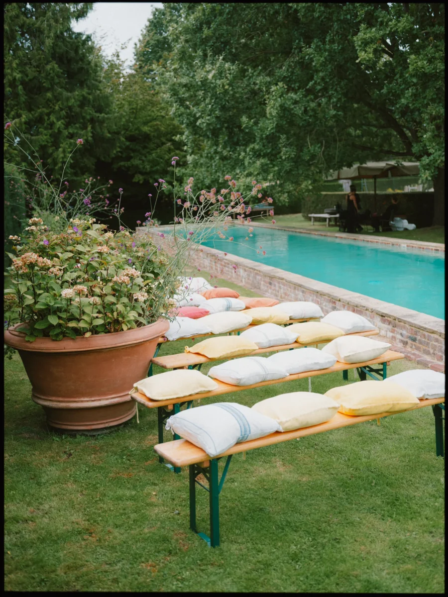Beer-garden benches with colorful cushions on the lawn beside a turquoise pool at Petersham Nurseries