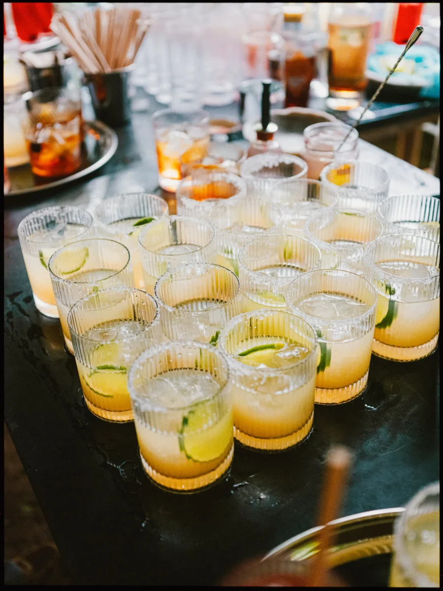 Rows of ribbed glasses filled with lime cocktails lined up on a dark bar, ready for guests to enjoy