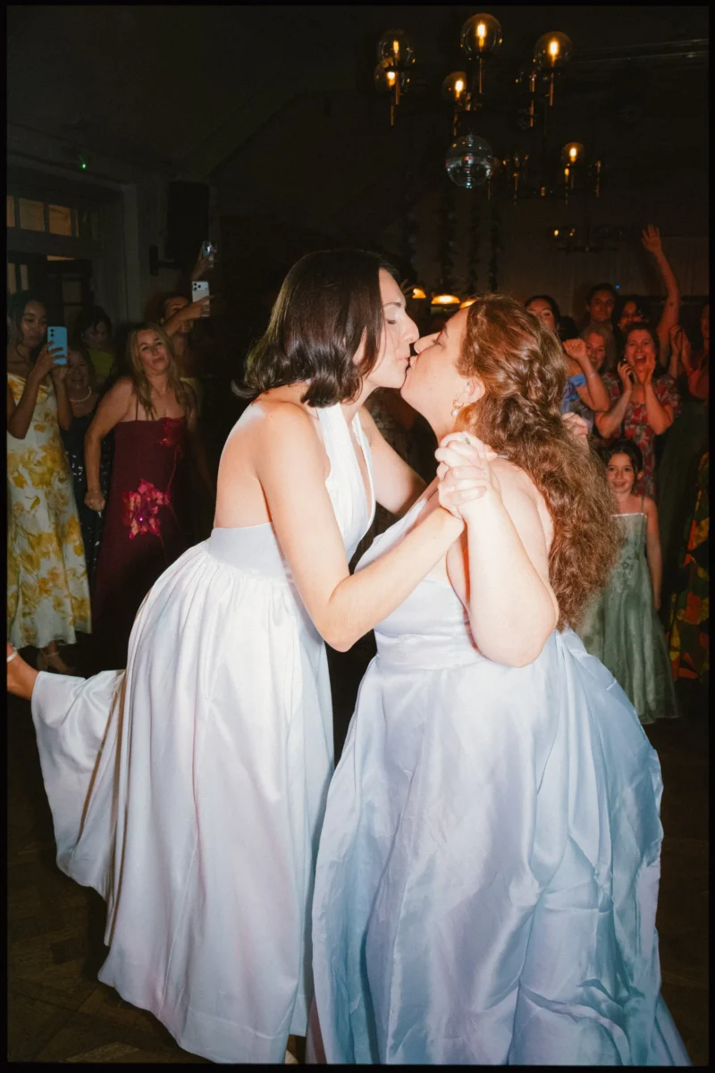 Two brides share a kiss mid-dance while guests cheer and film on their phones at The Turk's Head