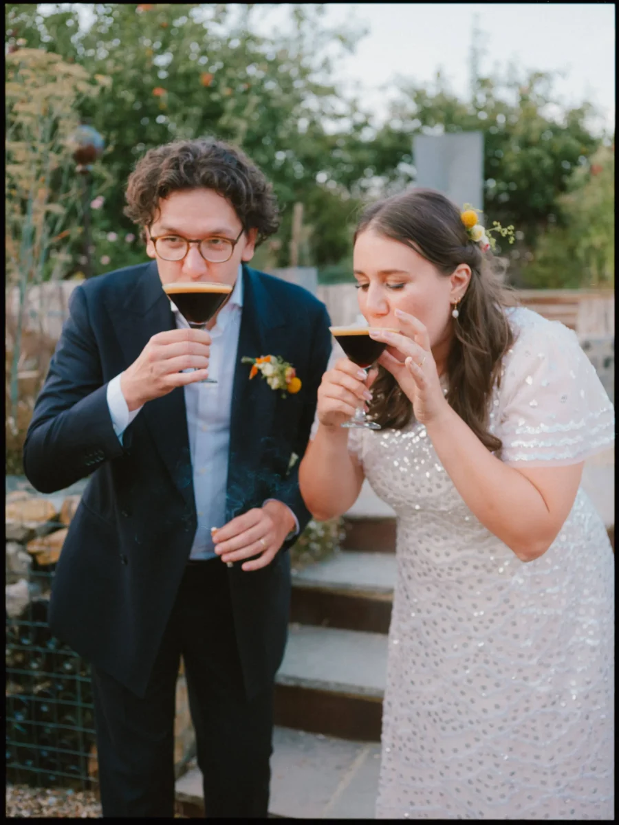 Maya and Lukas drink espresso martinis side by side on the garden steps at The Bell, caught mid-sip