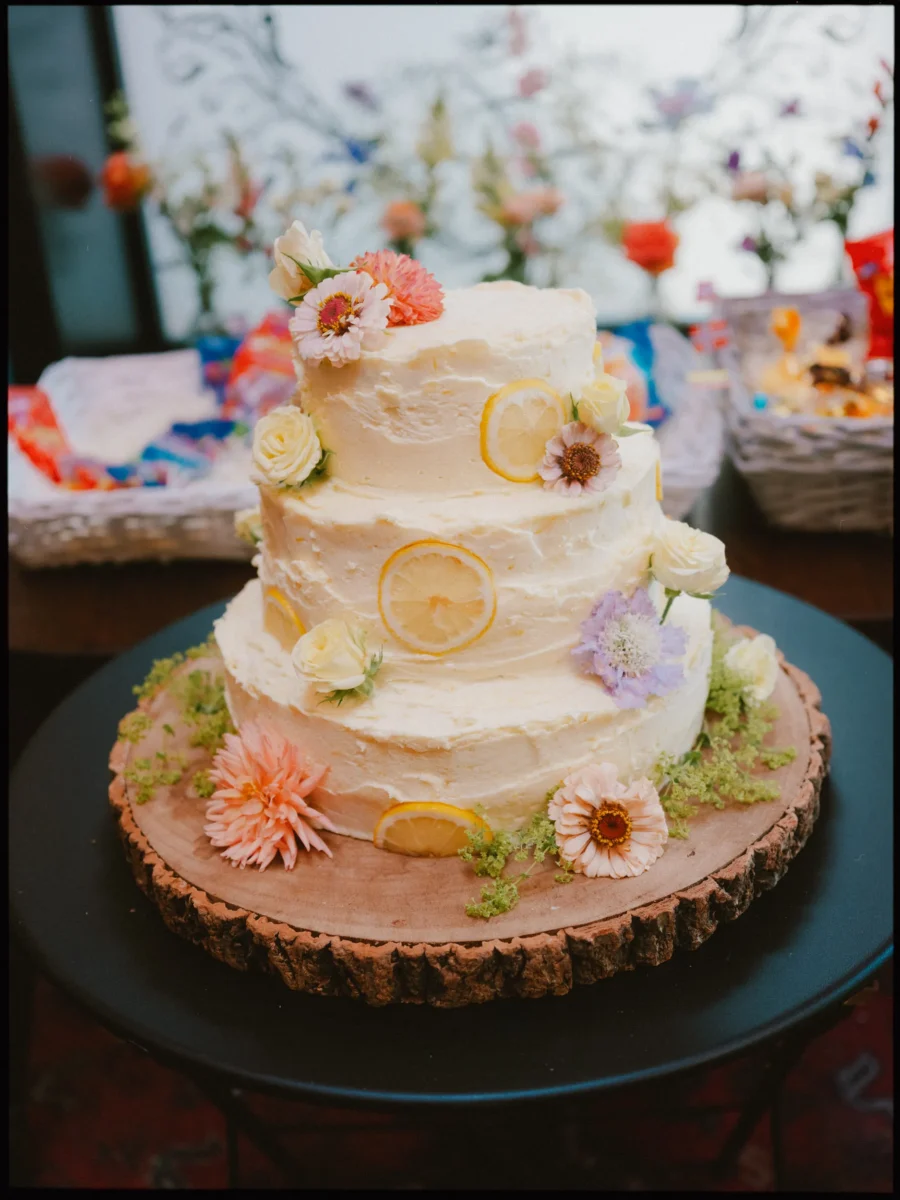 Three-tier buttercream wedding cake decorated with fresh flowers and lemon slices on a log slice stand at The Bell