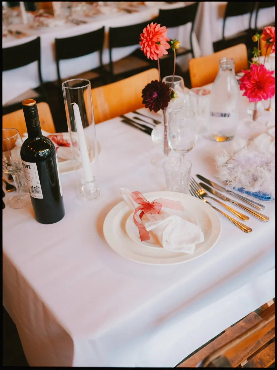 Place setting with a napkin tied in sheer red ribbon, gold cutlery, a taper candle and dahlias at Coin Laundry