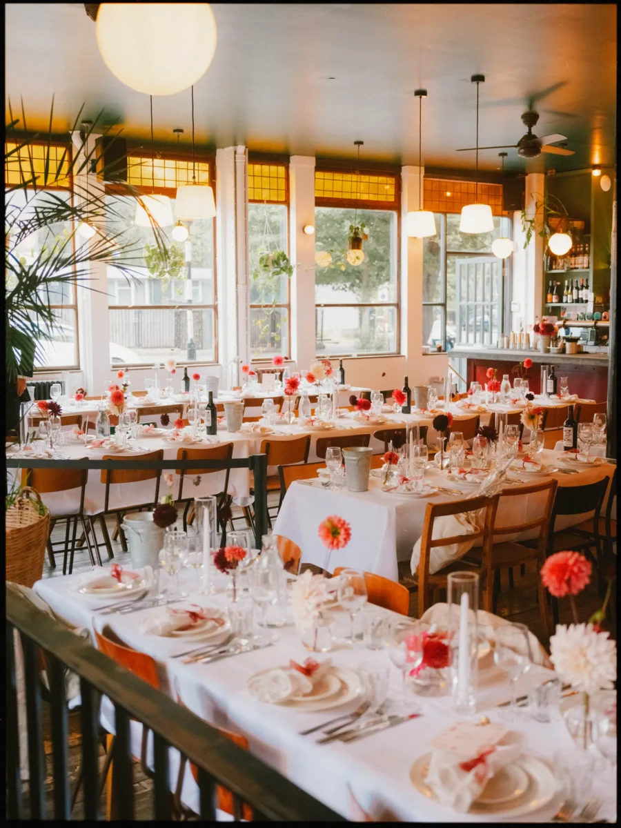 Long white-clothed tables dressed with red and pink dahlias, candles and napkins, ready for dinner in the sunlit Coin Laundry