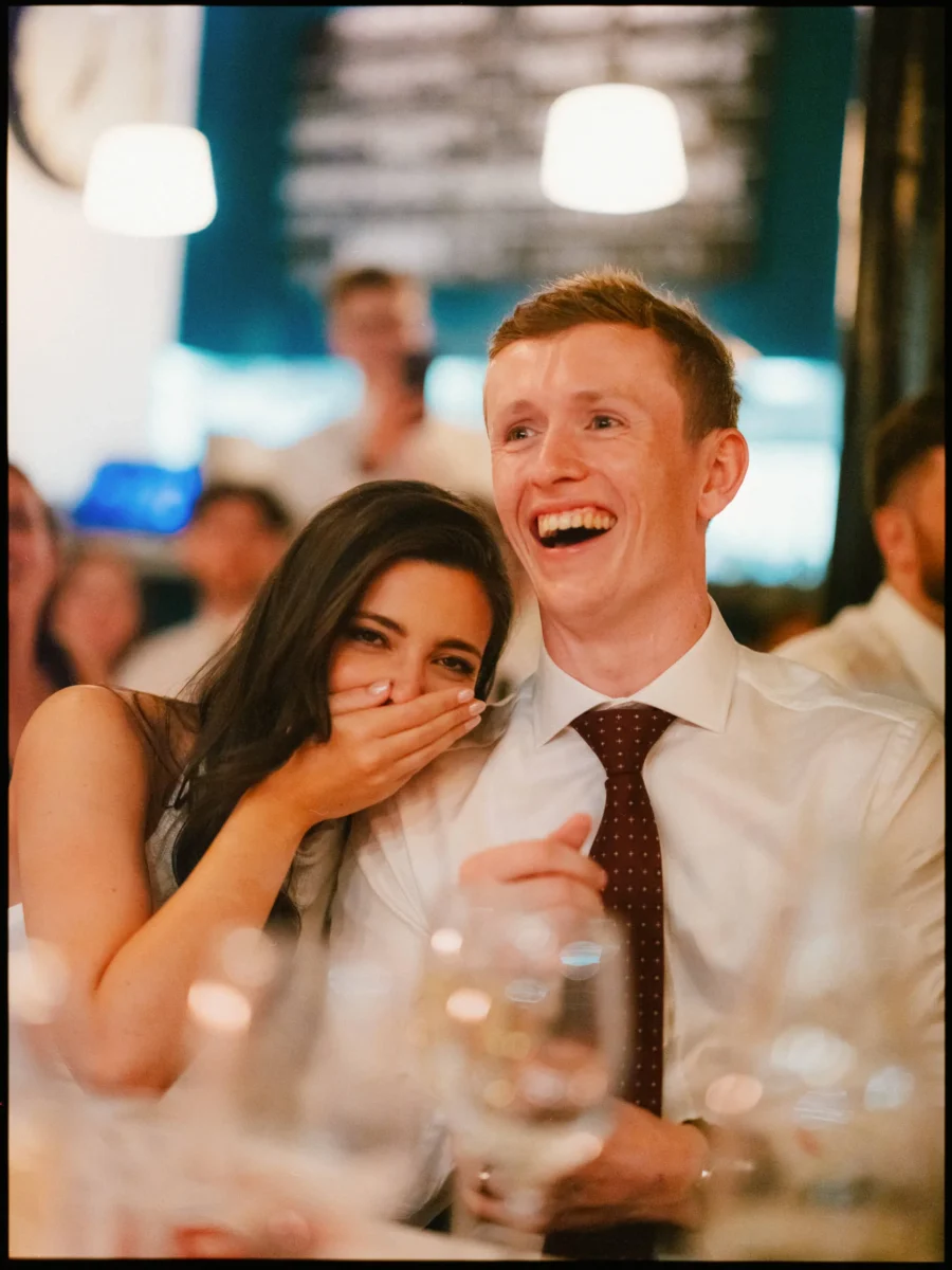 Guest covers her mouth in delighted shock as the man beside her laughs out loud at dinner in Coin Laundry
