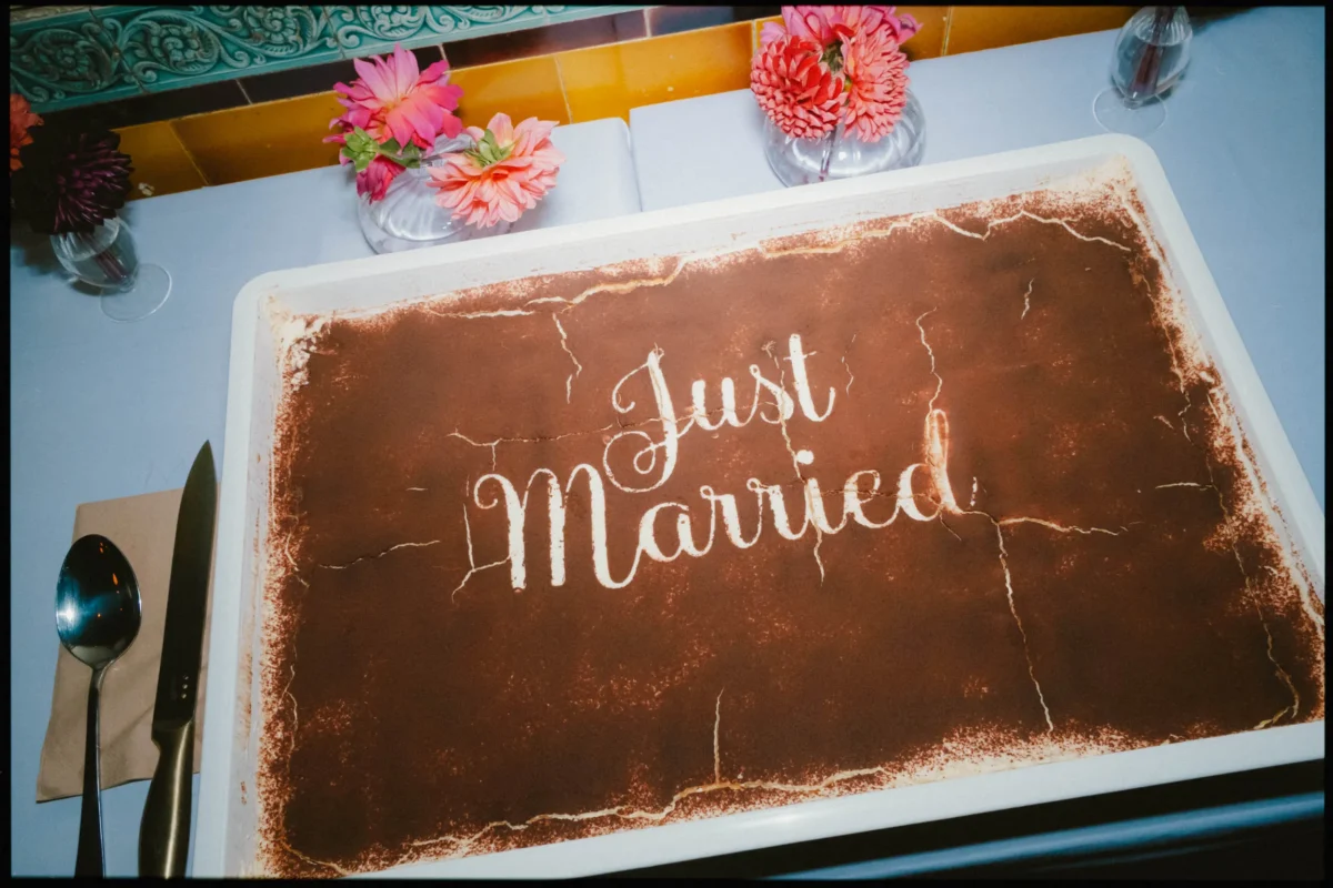 Tiramisu in a white tray dusted with cocoa and stencilled 'Just Married', beside pink dahlias at Coin Laundry
