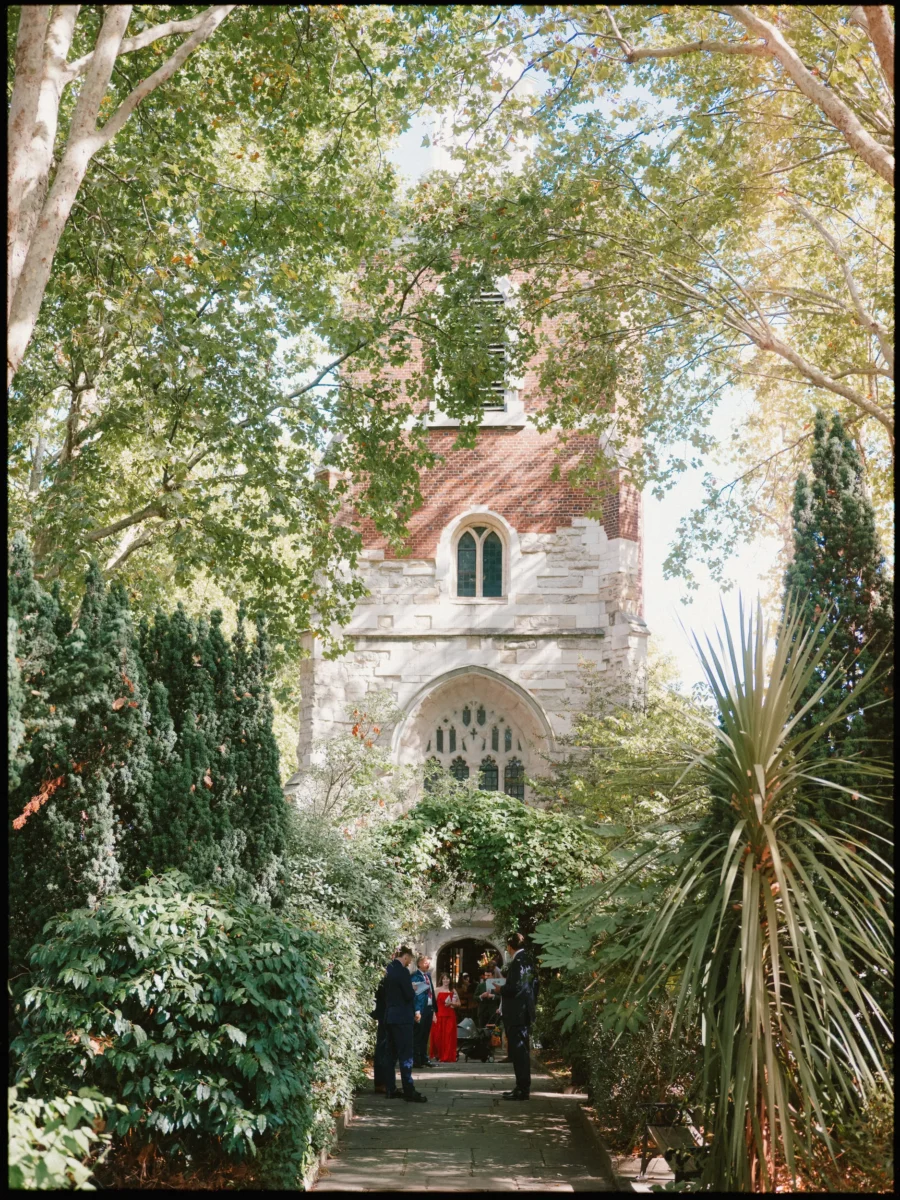 Wedding guests gather in a doorway at the foot of Bow Church's brick and stone tower, framed by leafy trees