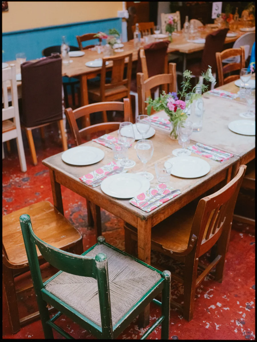 Wooden tables laid with white plates, floral napkins and wild flowers, mismatched chairs at Frizzante, Hackney City Farm