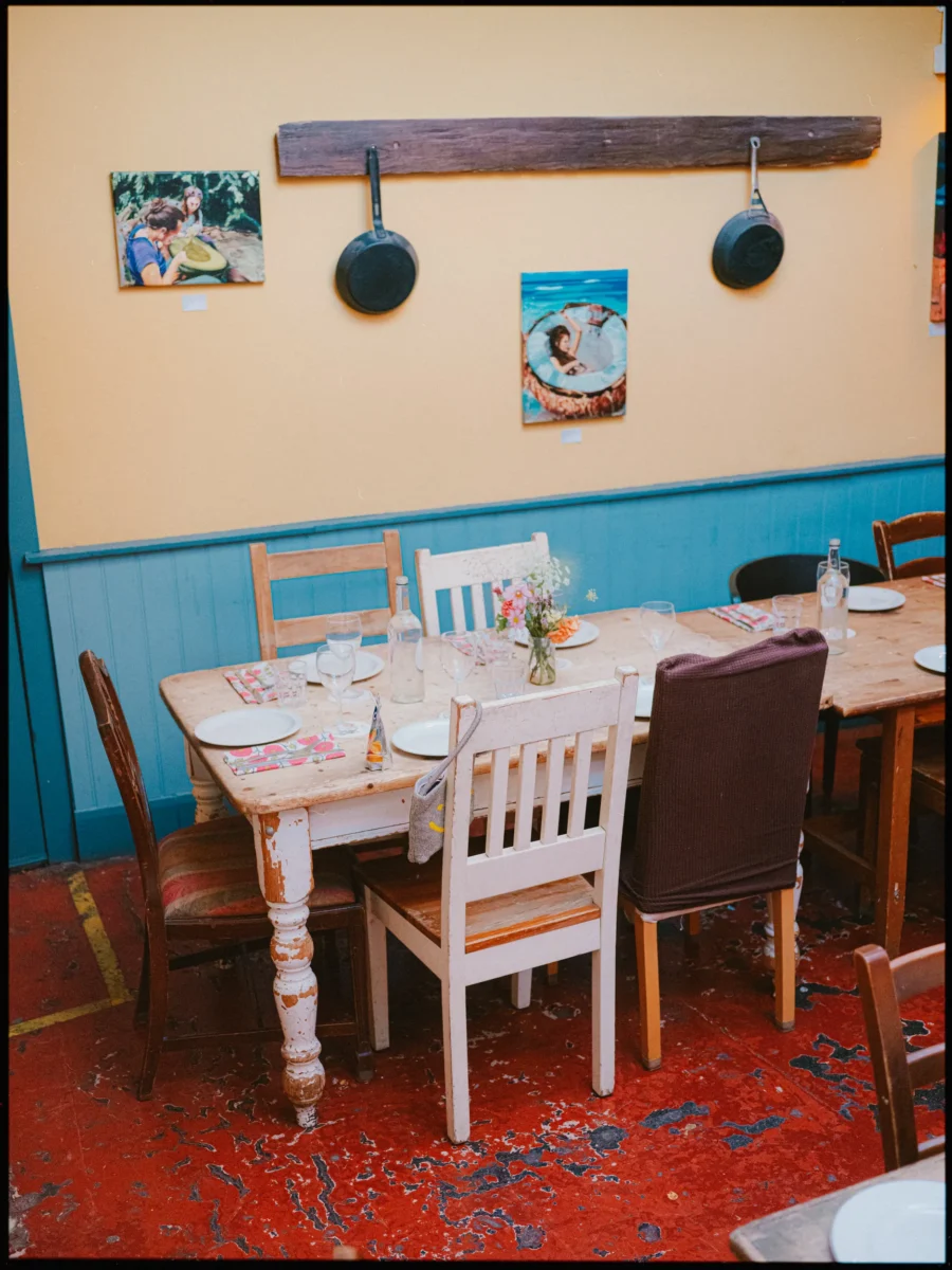 Rustic wooden table set with plates, floral napkins and a small posy, beneath cast iron pans and paintings on a yellow wall
