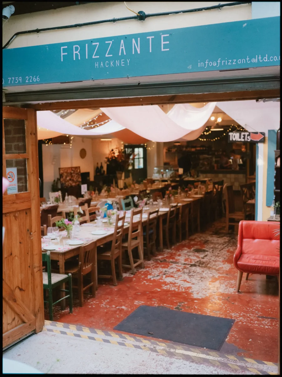Long wedding tables laid under draped white fabric and fairy lights inside Frizzante, seen through the open doorway