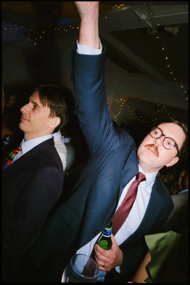 Guest with a moustache and glasses throws one arm up, beer in hand, on the crowded dance floor at Frizzante