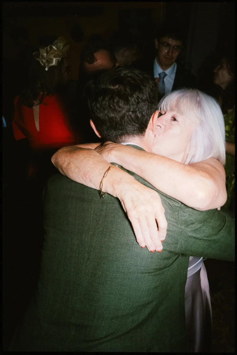 Woman with silver hair wraps her arms round a man in a green jacket during the dancing at Frizzante, guests behind