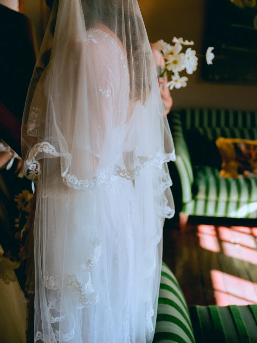 Lace-edged veil falling down the bride's back beside green striped sofas in a sunlit room at The George