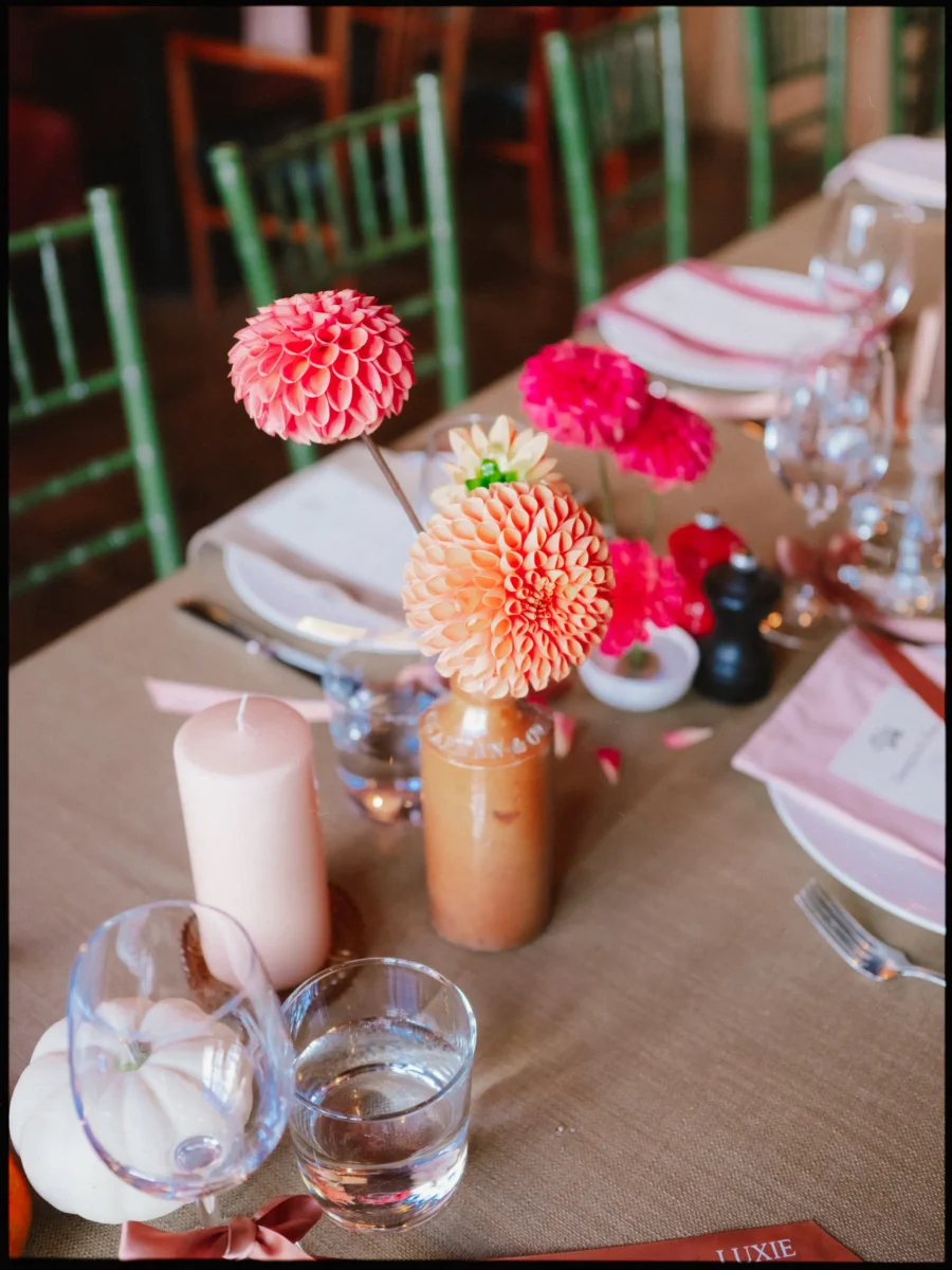Pink and peach dahlias in small stoneware bottles on a hessian-topped table with green chairs at The George in Rye
