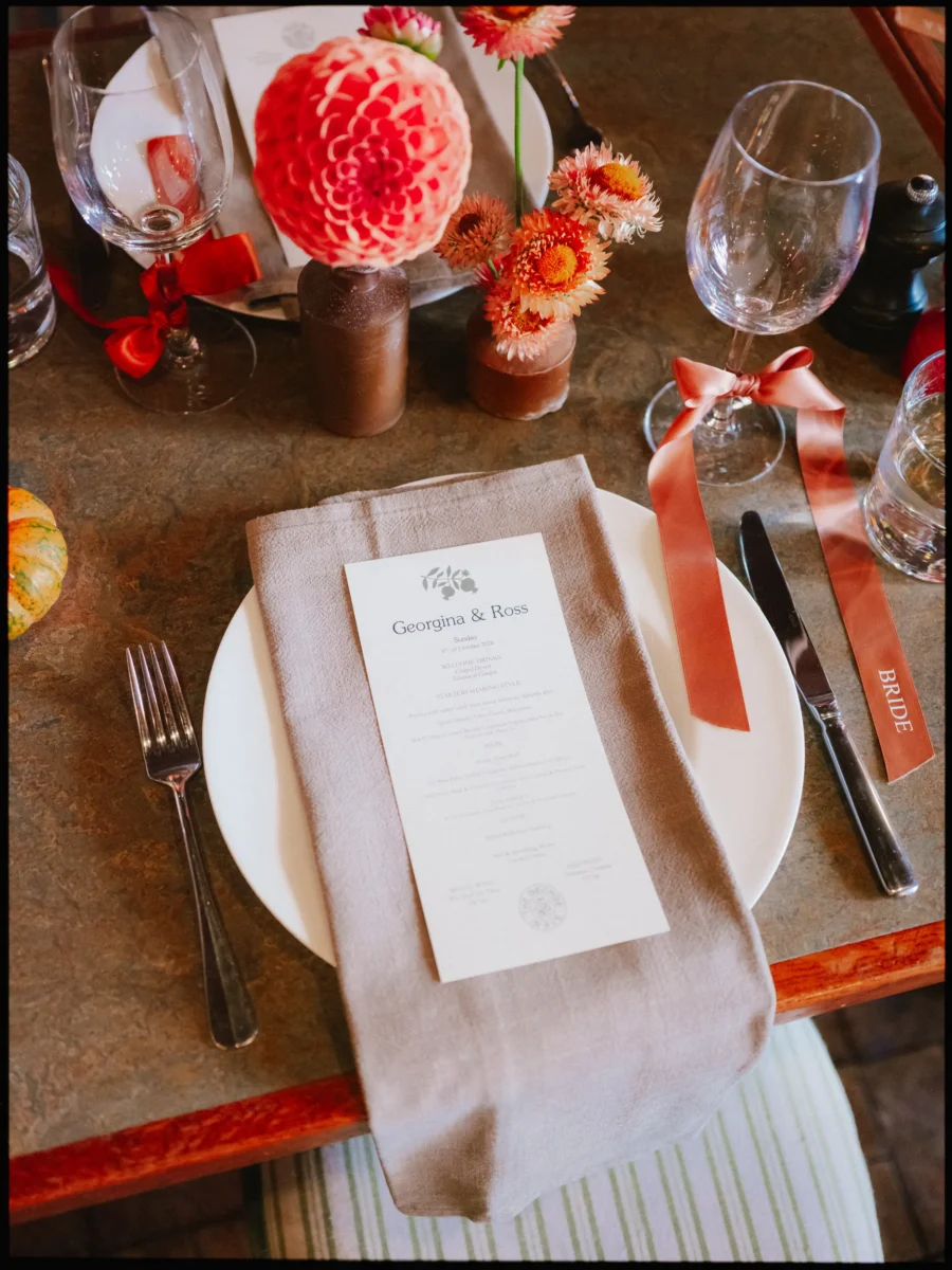 Bride's place setting with a Georgina & Ross menu on a linen napkin, dahlias and a terracotta ribbon at The George