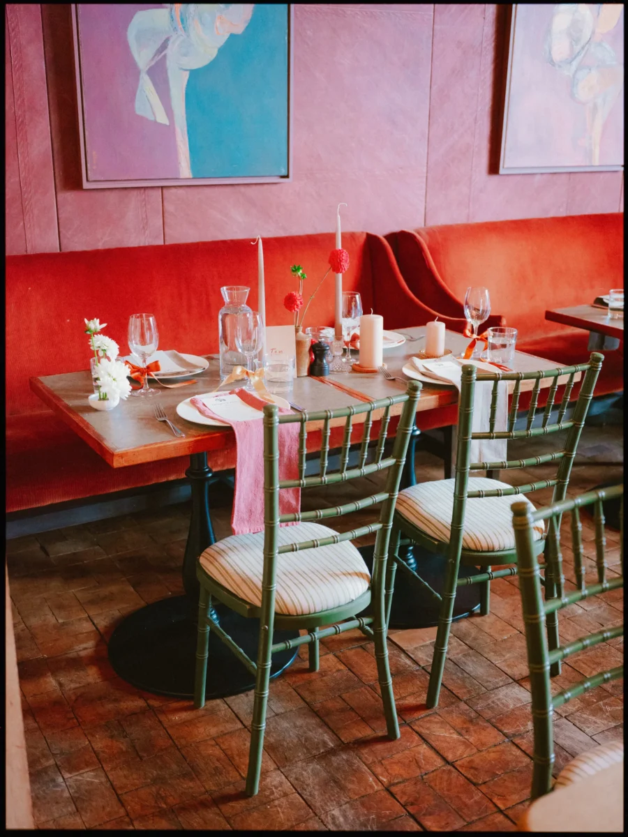 Wedding table set with pink napkins, orange ribbons and candles beside a red velvet banquette and green chairs at The George