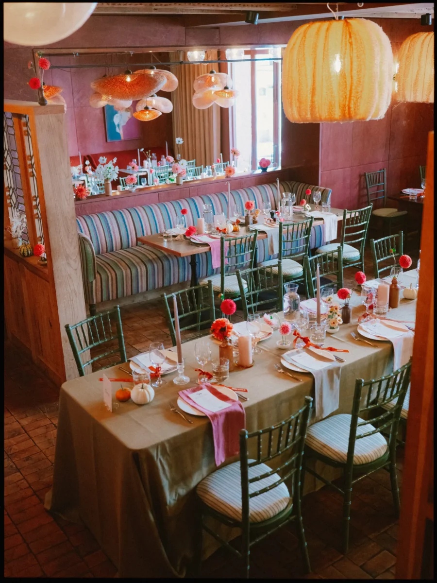 Wedding tables dressed with pumpkins, dahlias and orange ribbon, striped banquette and glowing paper lanterns beyond