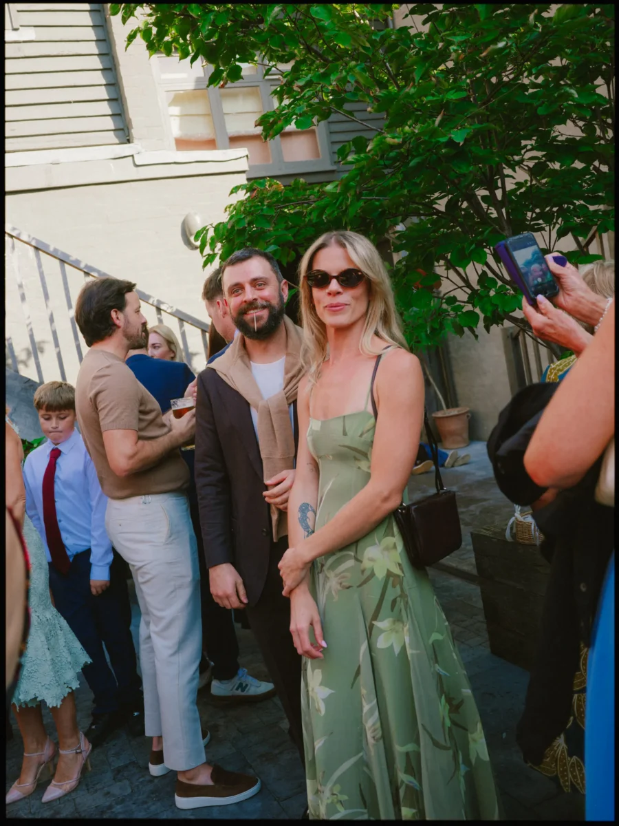 Guest in sunglasses and a green floral dress beside a smiling bearded man in the cobbled courtyard at The George