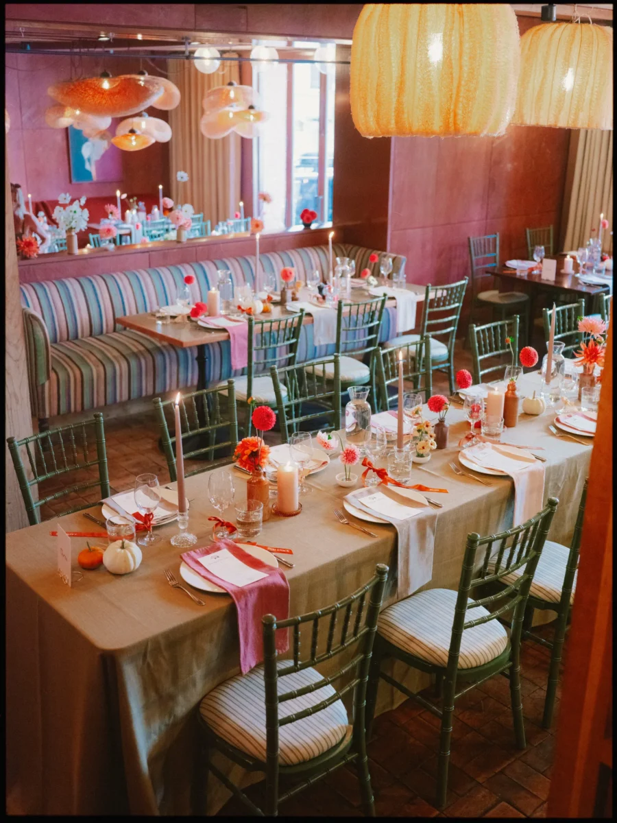 Long dinner table with green chairs, pink napkins, orange ribbons and taper candles under paper lanterns at The George