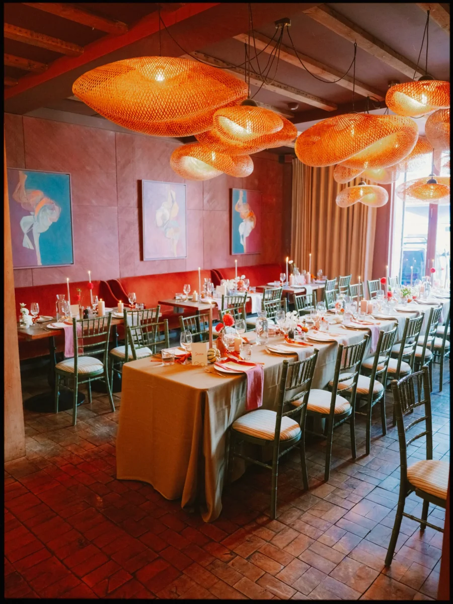 Long wedding table with candles and orange rattan pendant lights in a red-toned dining room at The George in Rye