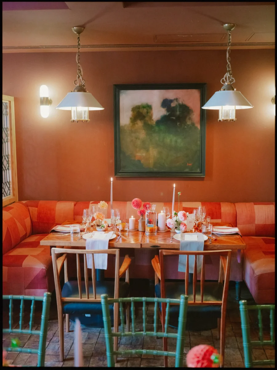 Wedding table laid for dinner with candles and pink dahlias on a patchwork orange banquette at The George in Rye