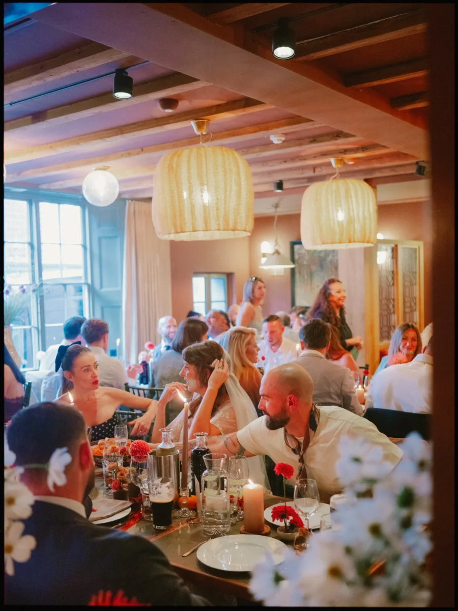 Guests laughing around a candlelit dinner table under woven pendant lights at The George