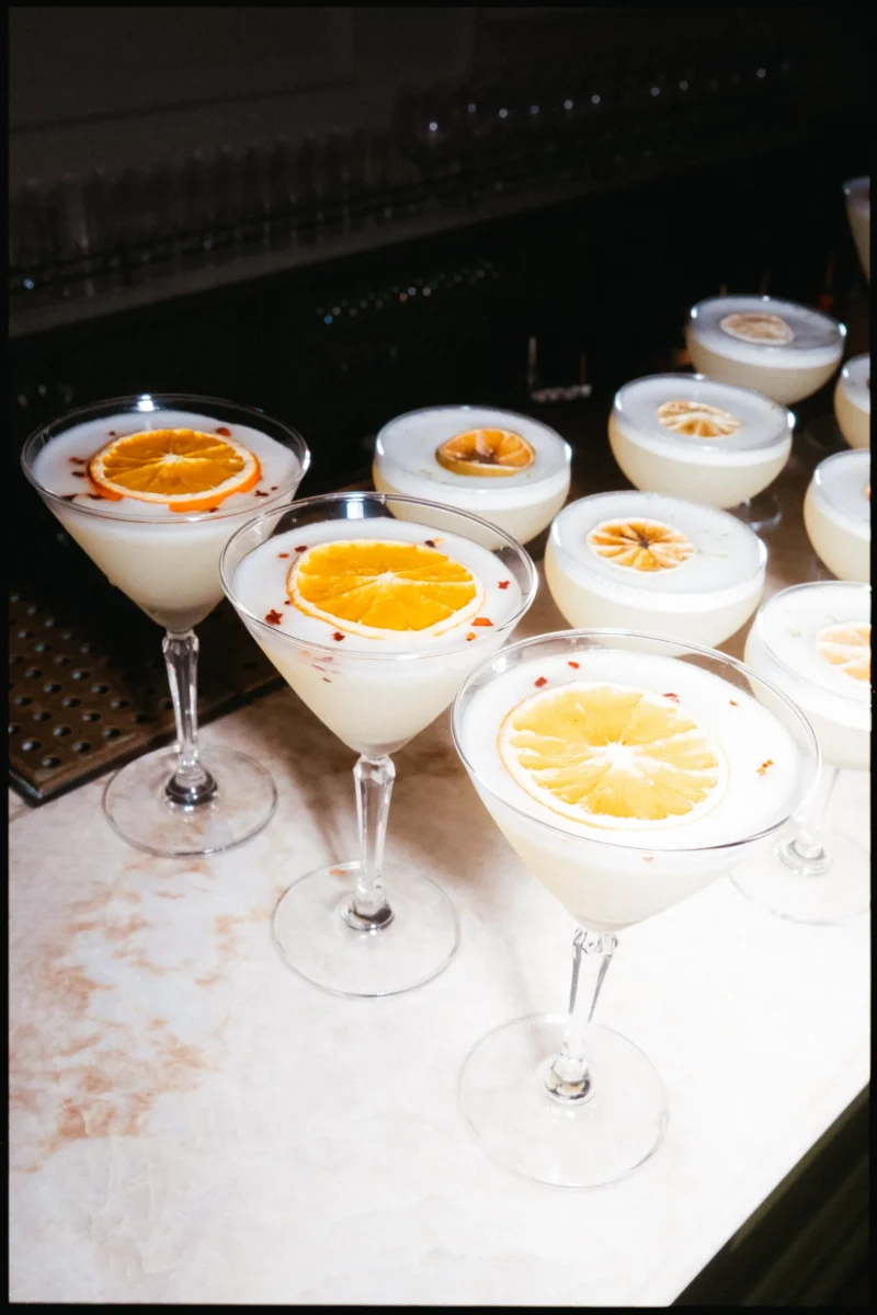 Row of creamy cocktails topped with dried orange slices lined up on the bar for the Ballroom party at The George