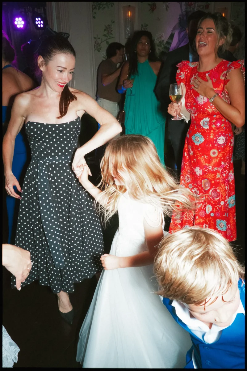 Woman in a polka dot dress holds hands with a twirling flower girl as guests laugh and dance in The George Ballroom