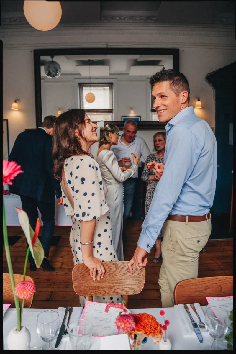 Smiling couple share a joyful moment as guests mingle behind them in the upstairs room at Camberwell Arms