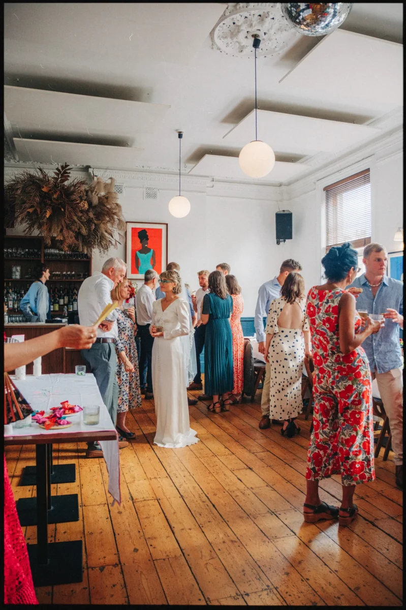 Guests in bright summer prints chat over drinks beside the bar and a disco ball at Camberwell Arms