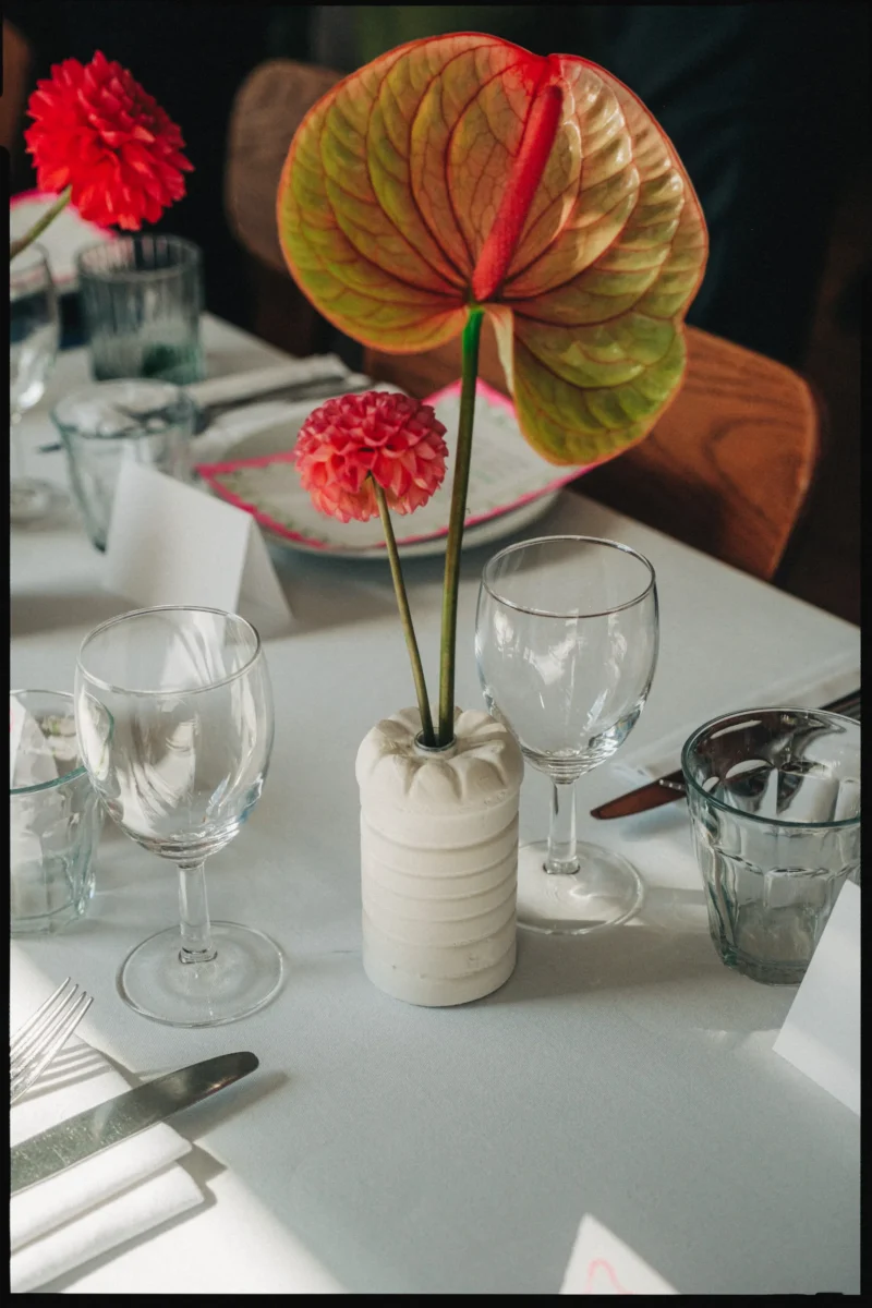 Green and orange anthurium and a coral dahlia in a ribbed white vase on a laid table at Camberwell Arms